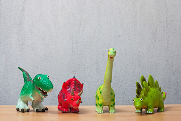 Four dinosaurs toys standing on a wooden floor.