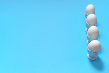 White eggs standing on egg cup isolated on blue background, copy space. Row of boiled eggs in stand. Healthy food concept. Easter eggs. Happy Easter concept