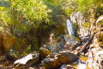 Young woman in a bikini stands on rock waterfall