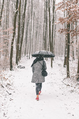 Frau läuft im Winter durch den Wald mit Regenschirm