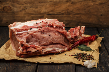 Fresh pork raw meat on a paper with spices on a dark wooden table. A piece of pork meat close-up. The meat is fresh. Selective focus.