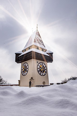 Naklejka premium Sun flares over snowy Uhrturm clocktower landmark of city Graz