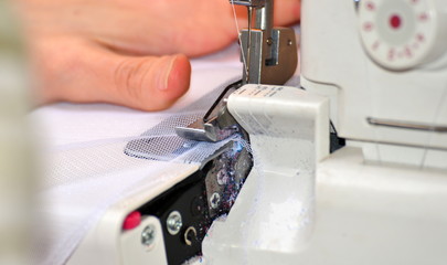 The woman at the sewing machine processes a white fabric, on manufacture close-up of a hand.