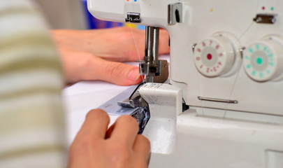 The woman at the sewing machine processes a white fabric, on manufacture close-up of a hand.