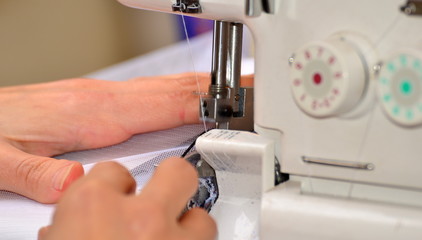 Naklejka premium The woman at the sewing machine processes a white fabric, on manufacture close-up of a hand.