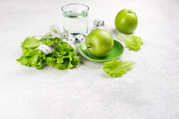 Healthy eating and diet background. Green apple, lettuce salad, glass of water, measuring tape. Dieting, slimming, weight loss concept. Top view. Copy space
