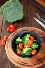 Broccoli cooked with cherry tomatoes inside a frying pan.