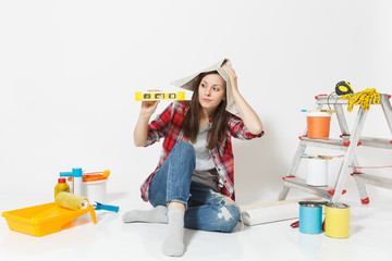 Woman in newspaper hat sitting on floor with bubble spirit level, instruments for renovation apartment isolated on white background. Wallpaper, gluing accessories, painting tools. Repair home concept.