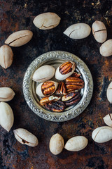Pecan nuts on metal plate over black rustic surface.