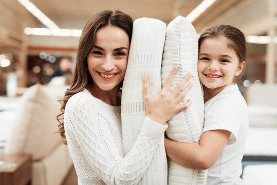 Smiling little girl with beautiful mother hugs pillows in store of orthopedic mattresses.