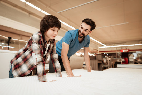 Tidy bearded father with young son is testing mattress for softness.