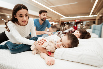 Young parents wake sleeping children on mattress in orthopedic furniture store.