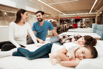 Young lovely couple is sitting on mattress next to sleeping children in furniture store.