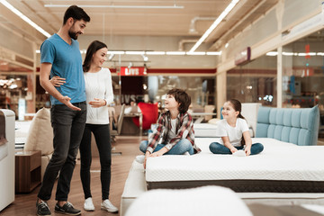 Happy family with children came in furniture store to buy mattress. Choosing mattress in store
