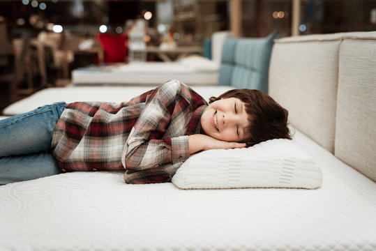 Joyful little boy lies on orthopedic pillow in mattress store. Check for softness of orthopedic furniture