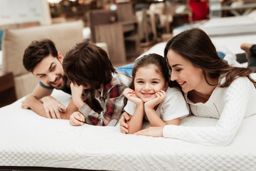 Young happy family checks on softness of orthopedic mattress, lying on bed in furniture store.