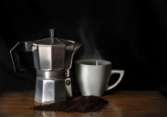 Italian coffee maker and a cup with hot drink over a wood table and a black background
