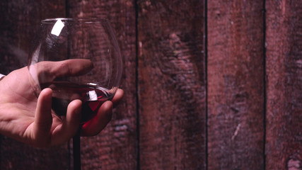 A crystal glass with red wine in hands, a background of wood.