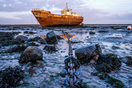 Rusty old fishing vessel marooned at low tide on a mud bank a long anchor chain