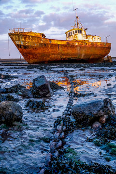 Rusty old fishing vessel marooned at low tide on a mud bank a long anchor chain