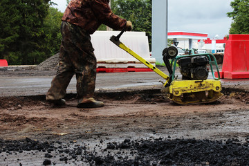 Fototapeta premium A road construction worker compacts the soil with a compact vibroplate before asphalting a problematic swampy section of the road. Russia, entry in the city of Gatchina