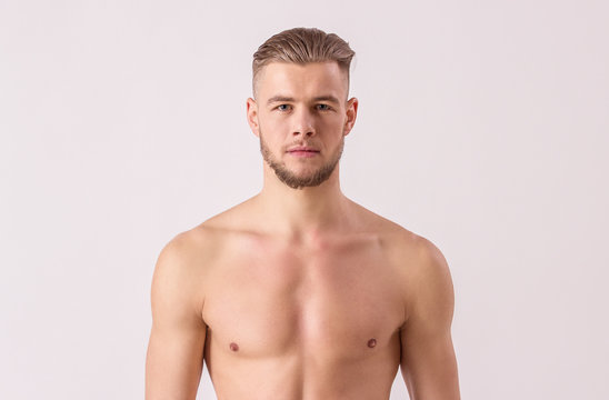 Studio shot of handsome naked man looking to camera while standing isolated on white background. Young bearded hipster standing against white background. Concept of men's masculinity and confidence