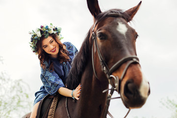 Fototapeta premium close-up of a cute girl with a wreath on her head sitting on a horse and smiling and stroking a horse's neck