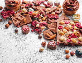 Chocolate with nuts, chocolate cupcakes and candies on grey background