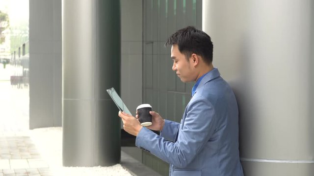 Asian young businessman reading tablet and drinking morning coffee