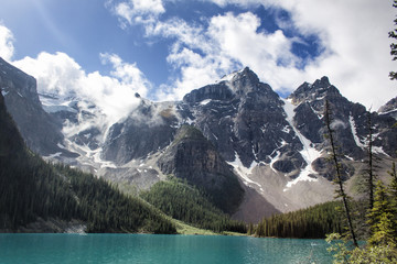 Fototapeta premium Standing on the shore with ice melt waters, mountain tops, trees and clouds
