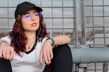 Young urban styled woman sitting next to industrial fence