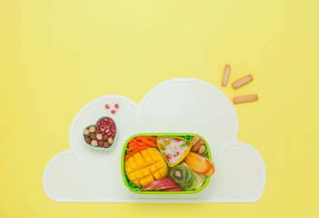 Lunch box with rice, fresh fruits and vegetables on the cloud napkin on yellow background
