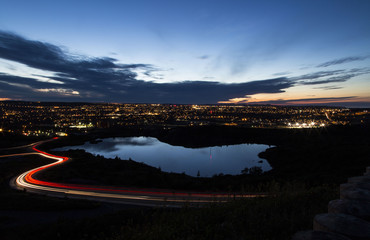light trails of cars overlooking a lake and a city at night