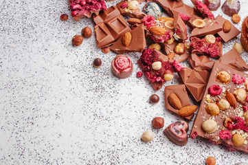 Pieces of chocolate with nuts and chocolate candies on grey background