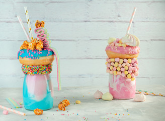 Two freak shakes topping with donut, popcorn and marmalade over brick background