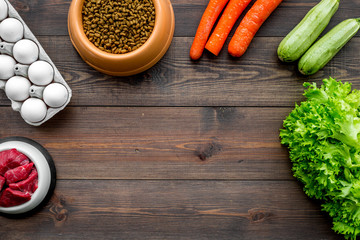 Dry pet food with natural ingredients. Raw meat, vegetables zucchini and carrot near eggs on dark wooden backgroud top view copy space