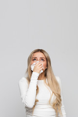 Studio portrait of unhealthy woman with napkin blowing nose, looking up to the source of the allergy. Copy space