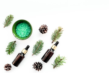 Pine spa cosmetics, products for skin care. Fir essential oil and green aromatic spa salt near branches and cones on white background top view copy space