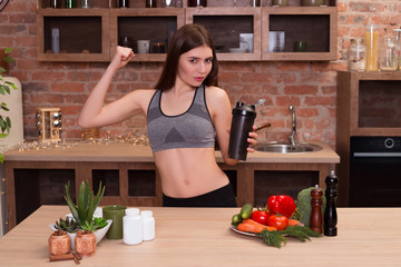 Take care of your body, its the only place you have to live. Young attractive strong woman with perfect naked torso showing shaker for sports nutrition in her kitchen.