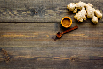 Spice and condiment. Ground ginger in small bowl near ginger root on dark wooden background top view copy space