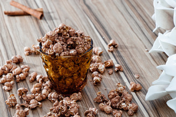 chocolate flavored popcorn in the yellow glass and on the brown wood table with cinnamon background