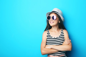 Portrait of beautiful girl with sunglasses and hat on blue background