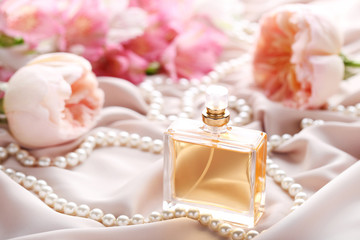 Fototapeta na wymiar Perfume bottle with roses and bead on satin background
