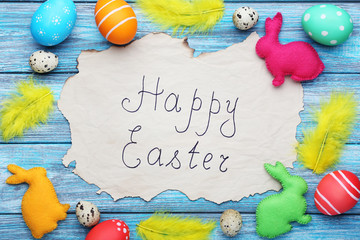 Obraz premium Inscription Happy Easter with painted eggs and fabric rabbits on wooden table