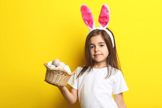 Beautiful little girl with rabbit ears and easter eggs on yellow background