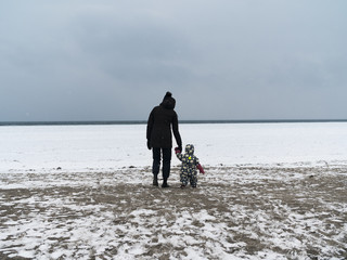 Woman and child holding hands wh8le walking on frosen snow covered beach towards the frozen ocean