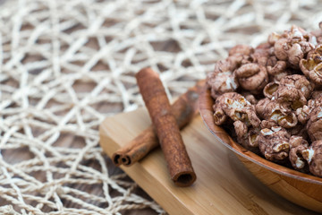 chocolate flavored popcorn in the yellow glass and on the brown wood table with cinnamon background