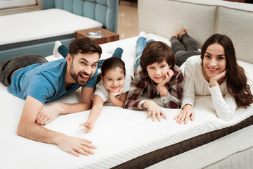 Happy family is relaxing on mattress in orthopedic furniture store. Big family check softness of...