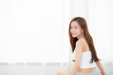 Beautiful asian young woman smiling with happiness leisure sitting on bed at home by the window, girl relax and wellness concept.
