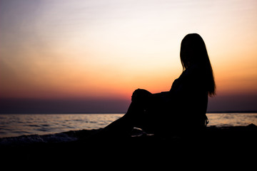 young girl at sunset in summer near the sea sits on the sand watching the sunset. silhouette at sunset